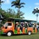 Passengers stepping off an open air tour bus in an area surrounded by tropical plants and trees